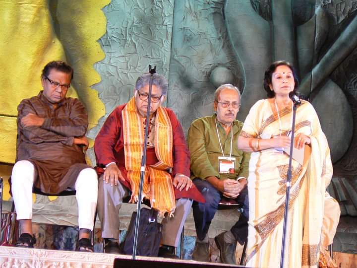 পিছনে বাঁ দিক থেকে সমরেশ মজুমদার, সুনীল গঙ্গোপাধ্যায় ও শীর্ষেন্দু মুখোপাধ্য়ায়। মাইকের সামনে লেখিকা।